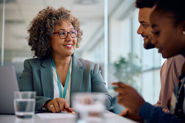 Happy real estate agent and young couple going through paperwork during meeting in office.