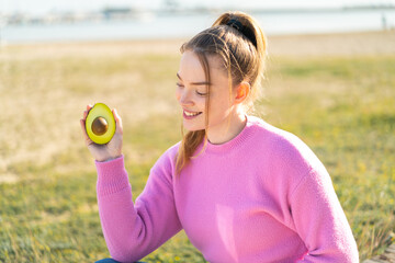 Poster - Young pretty girl holding an avocado at outdoors with happy expression