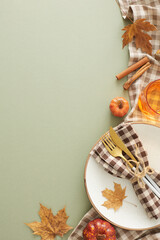 Autumnal table decor idea. Top view vertical shot of plate, cutlery, napkin, tablecloth, glass, cinnamon sticks, pumpkins, autumn leaves on olive background with empty space for advert or text
