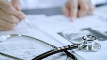 Professional Doctor Wearing Uniform Taking Notes In Journal, Physician Therapist Practitioner Filling Medical Documents On Clipboard Patient Form History And Prescription, Talking With Patient.