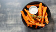 Sweet potato sticks in a black bowl served with white sauce, top view. Vegetarian food and healthy eating concept.