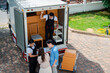 © Kiattisak - Asian Couple check while unloading boxes and furniture from a pickup truck to a new house with service cargo two men movers worker in uniform lifting boxes. concept of Home moving and delivery.