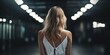 Mujer rubia de espalda en un almacén oscuro con luces desenfocadas, modelo de pasarela vista desde atrás 