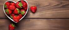 Top View Of A Ripe Garden Strawberry In A Heart-shaped Bowl Placed On A Wooden Table, With A Flat Lay Composition And Copy Space Available.