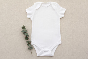 Wall Mural - Baby onesie flat lay on a linen fabric with eucalyptus. Baby bodysuit mockup. Copy space for your design here. Top view. Flat Lay.