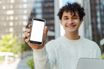 Young happy hispanic business man  holding smartphone using modern mobile app showing blank screen, selective focus, mockup. Technology concept