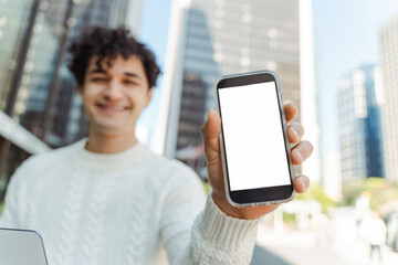 Young smiling latin man holding mobile phone showing blank screen, mockup. Technology, mobile app concept 