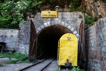 Entry gate to coal mine, leading deep into the earth. Mine shaft of the coal mine, near Despotovac city and Resavska Pecina, Serbia. Mining symbol on yellow wagon for coal excavation