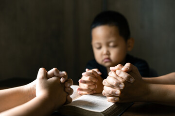 Christian family praying together concept. Child and mother worship God in home. Woman and boy hands praying to god with the bible begging for forgiveness and believe in goodness.