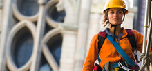 Brave Young Female Steeplejack In Safety Gear With Climbing Tools, Poised Beside Towering Historical Structure, Unique Perspective With Ample Blank Space. Generative AI