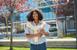 © insta_photos - Happy pretty female African American student walking outside university. Smiling cheerful girl model with curly hair wearing glasses, holding notebooks looking at camera outdoors, portrait.