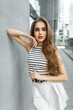 © alones - Fashionable beautiful cute young girl with red lips in trendy fashion summer casual outfit with a top and a skirt near a gray building in the city
