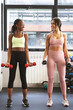 © JoseIMartin - two fitness women working out with weights in the gym while talking and smiling