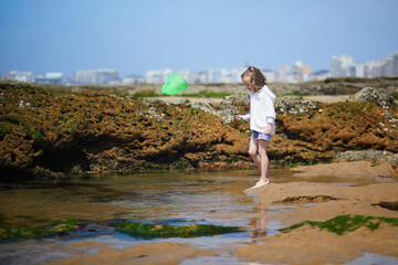 Wall Mural - Adorable preshooler girl playing with scoop net on the beach at Atlantic coast of Brittany, France