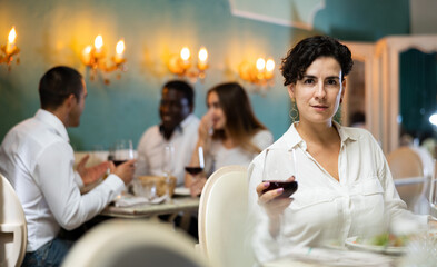 Wall Mural - Latino woman holding glass of red wine in cozy restaurant