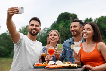 Sticker - Happy friends with glasses of cocktails taking selfie at table outdoors