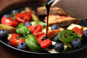 pouring balsamic vinegar onto fresh salad with blueberries, strawberries and basil on plate, closeup