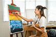 © Chanakon - Asian woman artist working on painting with brush and variant acrylic color. Female artist painter on canvas in creative studio as art concept