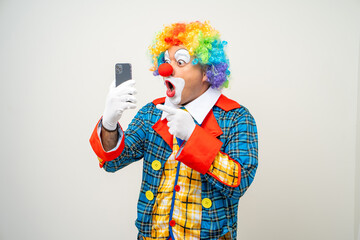 Wall Mural - Mr Clown. Portrait of Funny face Clown man in colorful uniform standing holding smartphone. Happy expression male bozo in various pose with cellphone on isolated background.