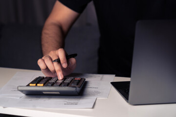 Wall Mural - Asian man is using a calculator to calculate his family's monthly miscellaneous expenses at home and record them in his laptop computer.