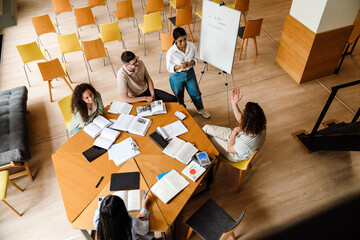 Top view of smiling woman making presentation for group of students at whiteboard in library