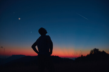 Wall Mural - man looking at the starry skies, crescent moon and shooting star in blue hour twilight time.
