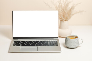 Laptop mockup with white screen, vase with pampas grass and cup of tea with lemon. Laptop background for study, work, cozy home office, web site promotion, online courses, autumn and winter theme