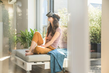 Young Woman Sitting At The Window At Home Wearing VR Glasses