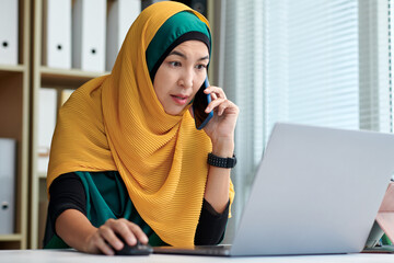 Wall Mural - Mature muslim businesswoman talking on phone with coworker when reading e-mails