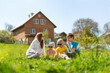 © somemeans - Mother and three children sitting on the grass in clearing with dandelions. Family picnic in backyard of house.