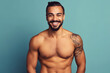 © NPix - Tattooed muscular brunette young man smiling at the camera on a blue background. Generative AI.