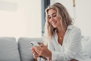 Portrait of one young attractive blonde woman using phone cell on couch relaxing surfing the net at home. Relaxing online concept lifestyle.