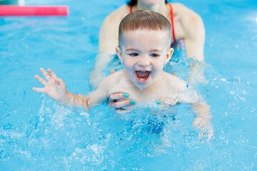 Wall Mural - A 2-year-old boy learns to swim in a pool with a coach. Swimming lessons for children. Swimming school for children. Educational swimming courses for children