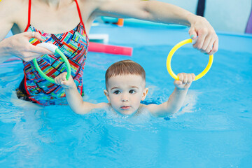 Wall Mural - A 2-year-old boy learns to swim in a pool with a coach. Swimming lessons for children. Swimming school for children. Educational swimming courses for children