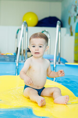 Wall Mural - Development for babies. A little boy is learning to swim in the pool. Children's first swimming lessons. Development for babies