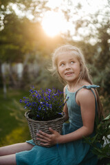 Wall Mural - Potrait of little girl holding wicker pot with flowers in the garden.