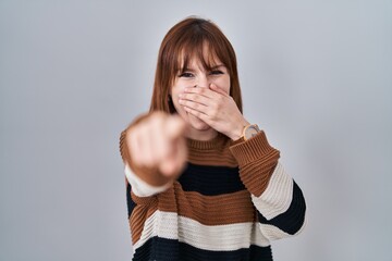 Canvas Print - Young beautiful woman wearing striped sweater over isolated background laughing at you, pointing finger to the camera with hand over mouth, shame expression