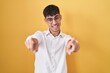 © Krakenimages.com - Young hispanic man standing over yellow background pointing to you and the camera with fingers, smiling positive and cheerful