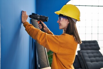 Poster - Young blonde woman wearing hardhat using dirll on wall at new home