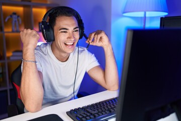 Young hispanic man streamer playing video game with winner expression at gaming room