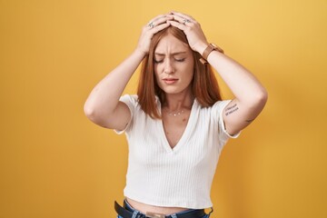 Poster - Young redhead woman standing over yellow background suffering from headache desperate and stressed because pain and migraine. hands on head.