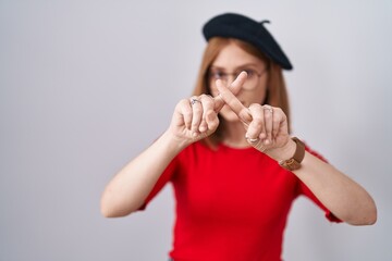 Wall Mural - Young redhead woman standing wearing glasses and beret rejection expression crossing fingers doing negative sign