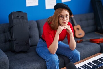 Sticker - Young redhead woman artist sitting on sofa with serious expression at music studio