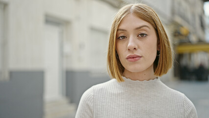 Poster - Young blonde woman standing with serious expression at street