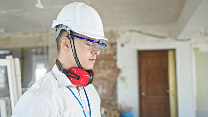 Poster - Young hispanic man architect wearing headphones standing with relaxed expression at construction site