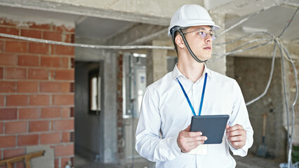 Poster - Young hispanic man architect standing with relaxed expression using touchpad at construction site