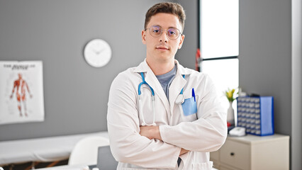 Wall Mural - Young hispanic man doctor standing with serious expression and arms crossed gesture at clinic