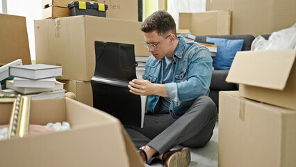 Sticker - Young hispanic man sitting on floor looking for paper on folder at new home