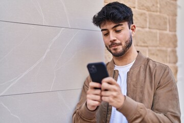 Wall Mural - Young hispanic man using smartphone at street