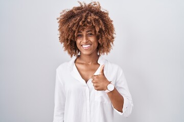 Sticker - Young hispanic woman with curly hair standing over white background doing happy thumbs up gesture with hand. approving expression looking at the camera showing success.